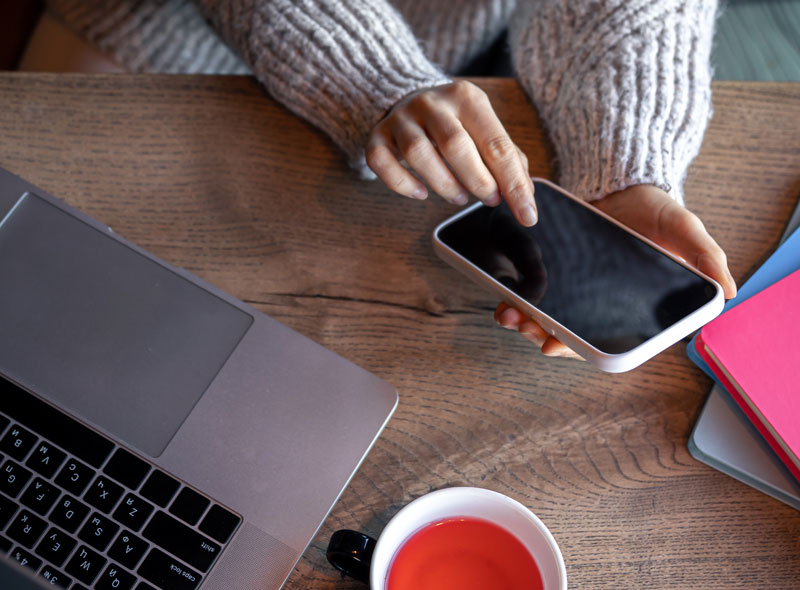 person on a mobile phone with a laptop and coffee mug